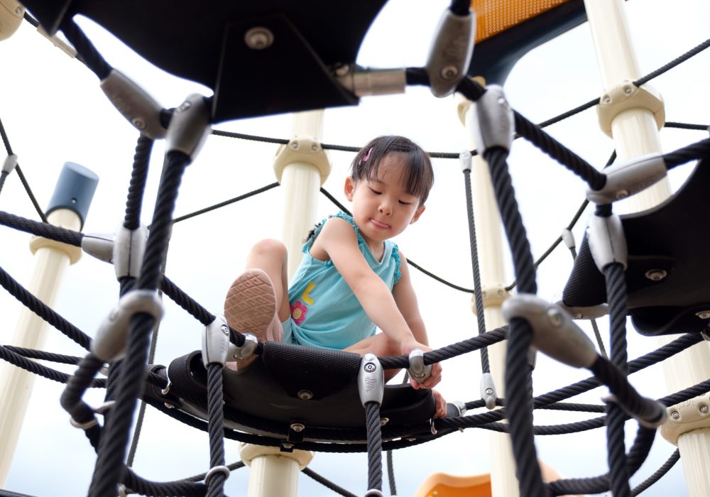 Active little Asian girl playing on the public playground